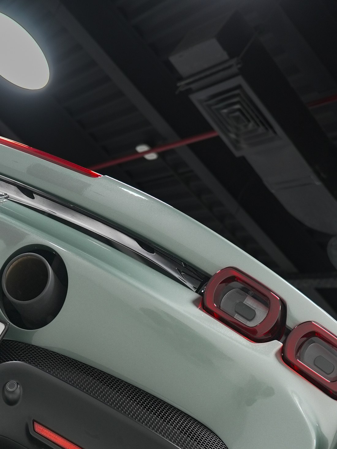 Carbon-bodied car detail under workshop lighting, rear three-quarter